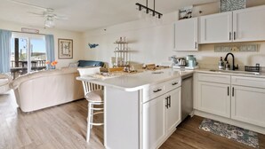 A modern kitchen with white cabinetry, a central island, and a dining area with a blue couch. - Studio with prime location next to Beach, Jolly Rogers and Boardwalk (Ocean City)