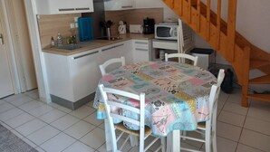 Eine kleine Küche mit weißen Schränken, einer Mikrowelle und einer Kaffeemaschine. Eine Holztreppe führt zu einer erhöhten Ebene.