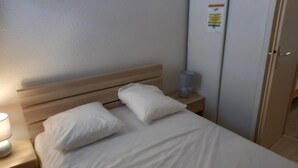 Ein ordentlich bezogenes Bett mit weißen Leinen und Kissen, eine Nachttischlampe und ein kleiner Tisch ebenfalls mit einer Lampe.