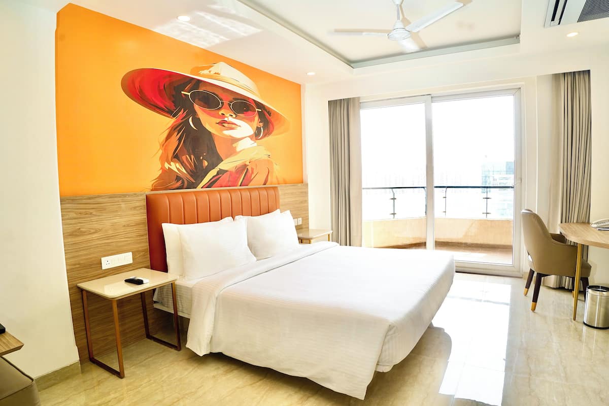 A hotel room with a large bed, a desk, and a balcony with a view.