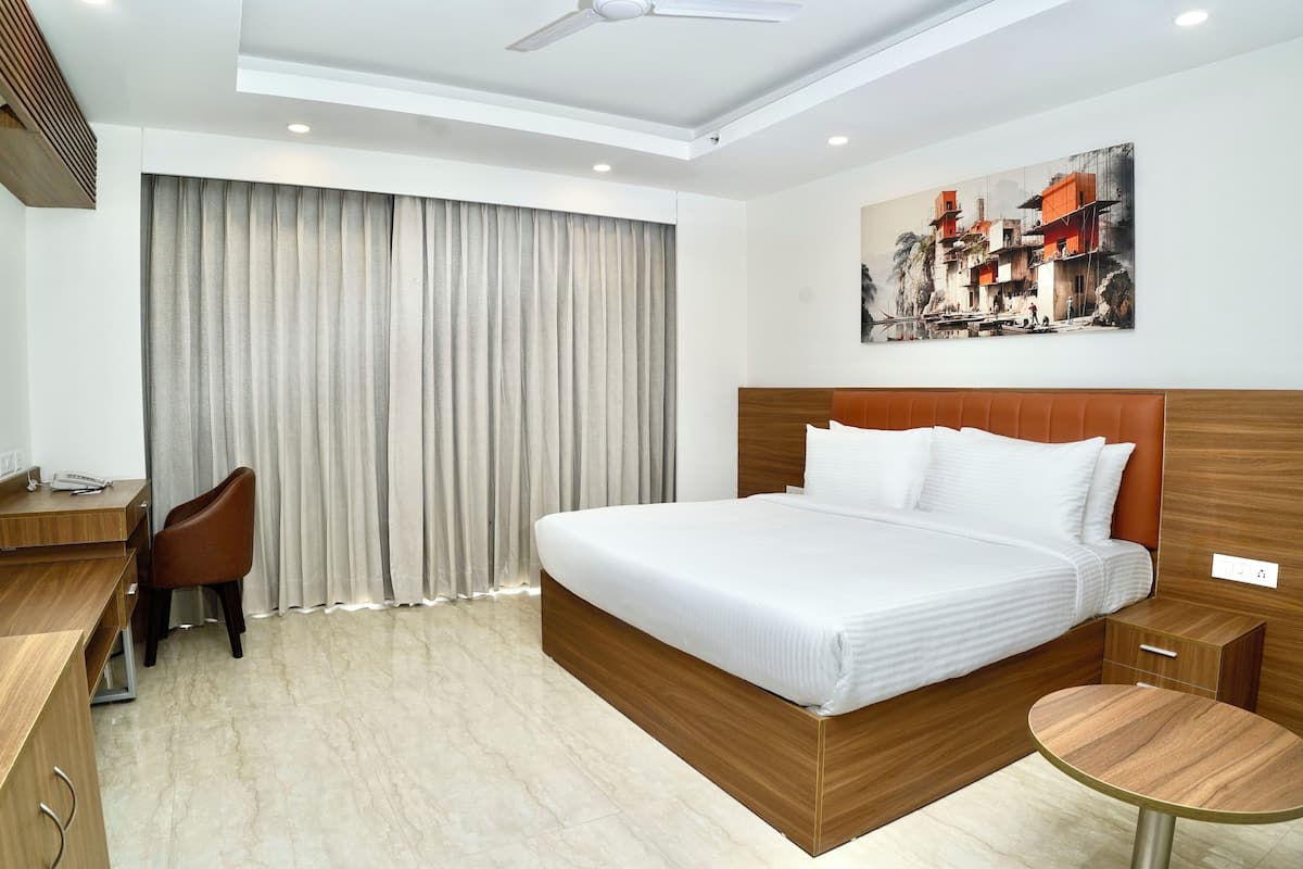 A hotel room with a large bed, a desk, a chair, a small table, and a painting on the wall.