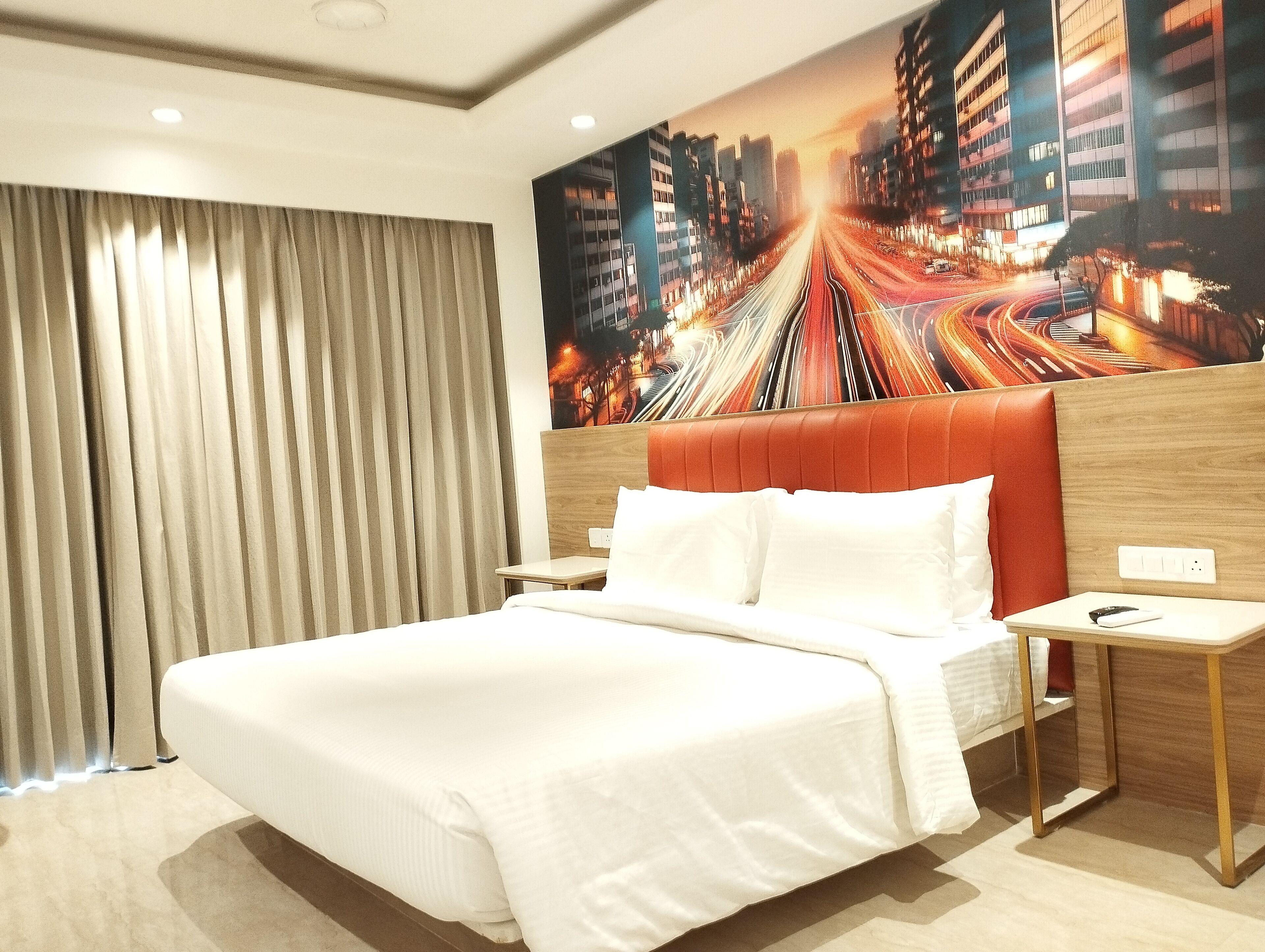 A hotel room with a large bed, a nightstand, a wall-mounted TV, and a window with curtains.