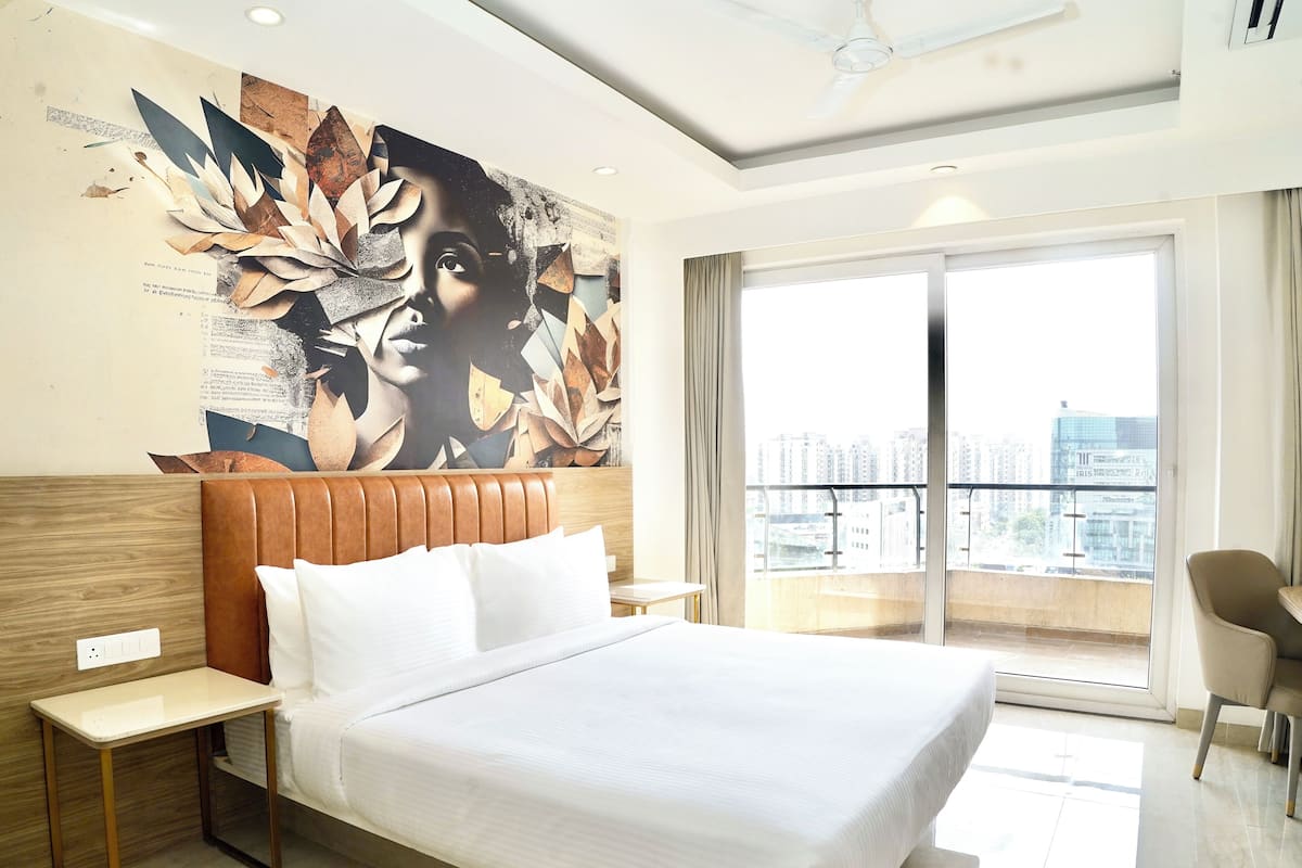 A hotel room with a large bed, a wooden headboard, a small bedside table, and a view of the city through a large window.