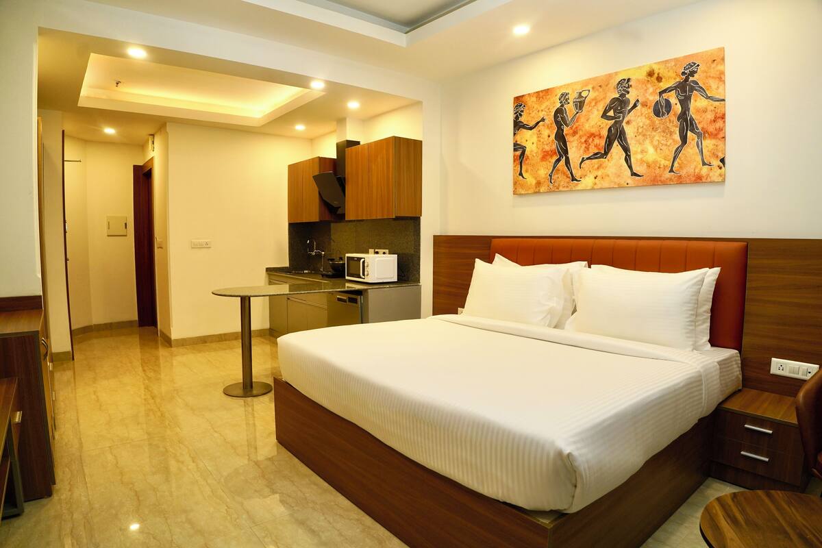 A hotel room with a large bed, a small kitchen area, and a dining table.