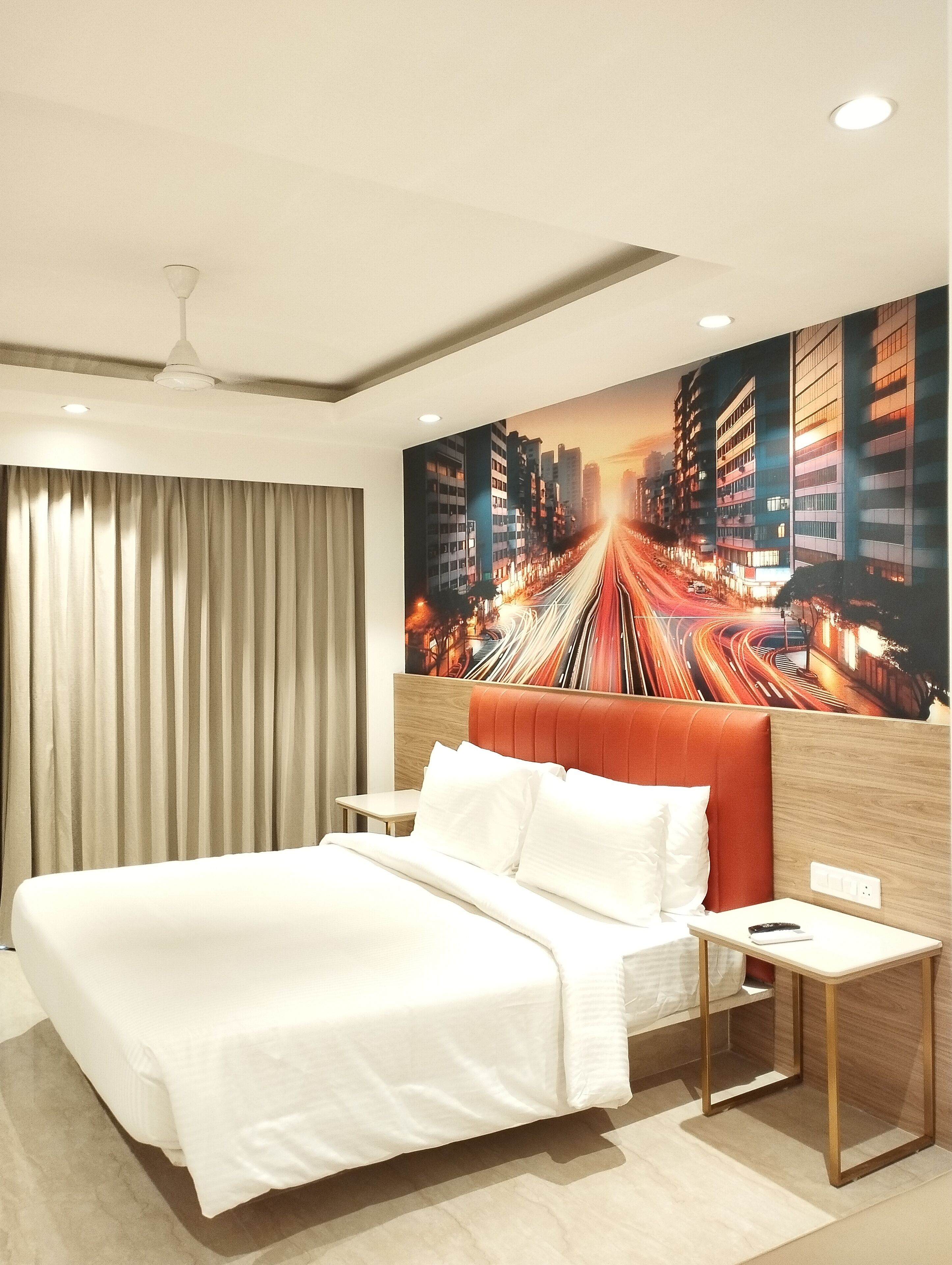 Une chambre d’hôtel moderne avec un grand lit, une table de chevet, un téléviseur fixé au mur et une fresque représentant un paysage urbain.