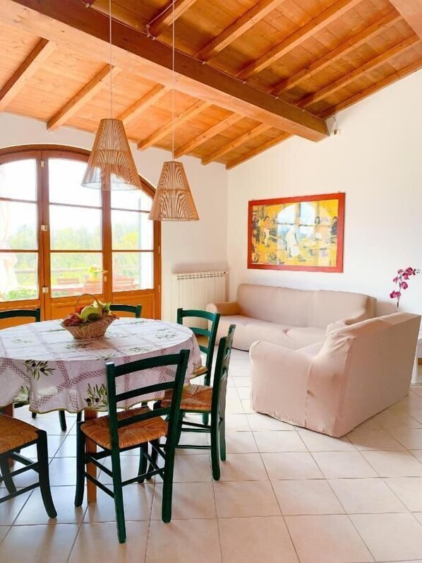 Un coin repas avec une table ronde, des chaises et des lampes suspendues. On y trouve également un canapé et un tableau au mur.