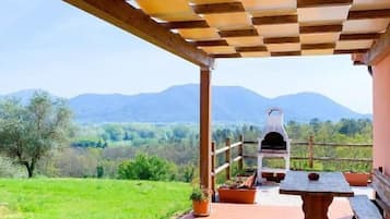 Relax in a serene outdoor space with a pergola overhead, a wooden table, and benches, perfect for al fresco dining amidst the scenic views of green fields and distant mountains.