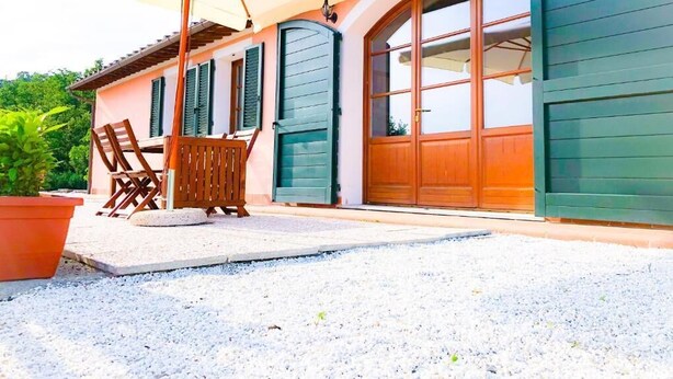 Une terrasse couverte, aménagée avec du mobilier d’extérieur, un grand parasol et une porte verte.