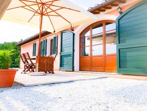 Une terrasse couverte, aménagée avec du mobilier d’extérieur, un grand parasol et une porte verte.