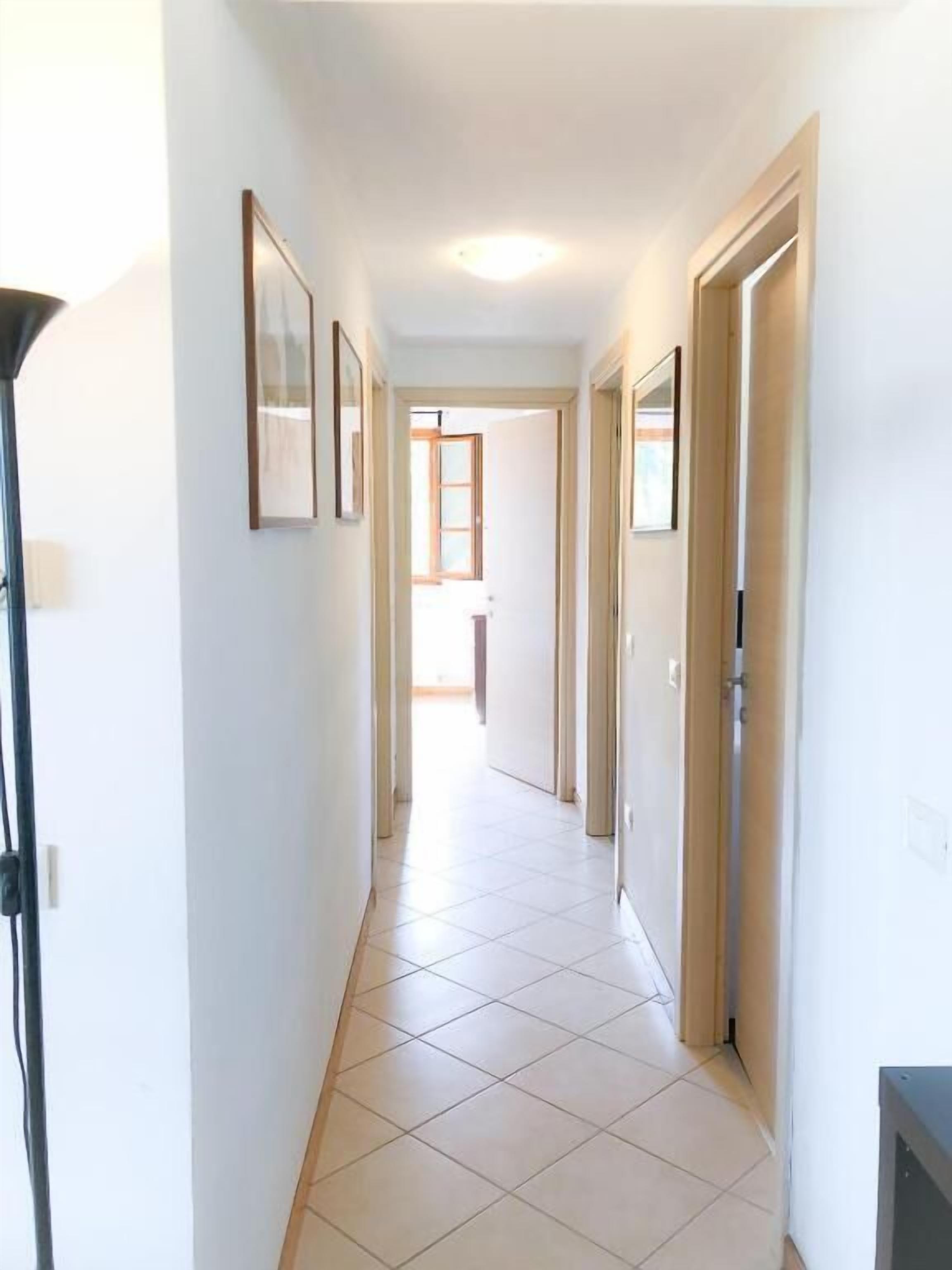 Un pasillo estrecho con suelo de baldosas, paredes blancas y puertas que dan a otras habitaciones.