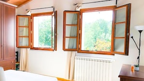 Une chambre à coucher comprenant un lit, un radiateur et deux fenêtres avec des cadres en bois et des vitres.