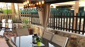 An outdoor patio with a glass table and chairs, a hanging light fixture, and a stone wall backdrop.