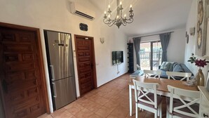 A kitchen with a refrigerator, a wooden door, a dining table with chairs, and a chandelier.