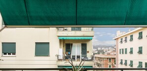 A balcony with a green awning, a white door, and a view of a cityscape with buildings and a hill in the background. - Bright Apartment in San Martino by Wonderful Italy (Genoa)