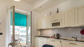 Eine Küche mit Blick auf Gebäude, ein Tisch mit Stühlen und ein Fenster mit einem grünen Vorhang.