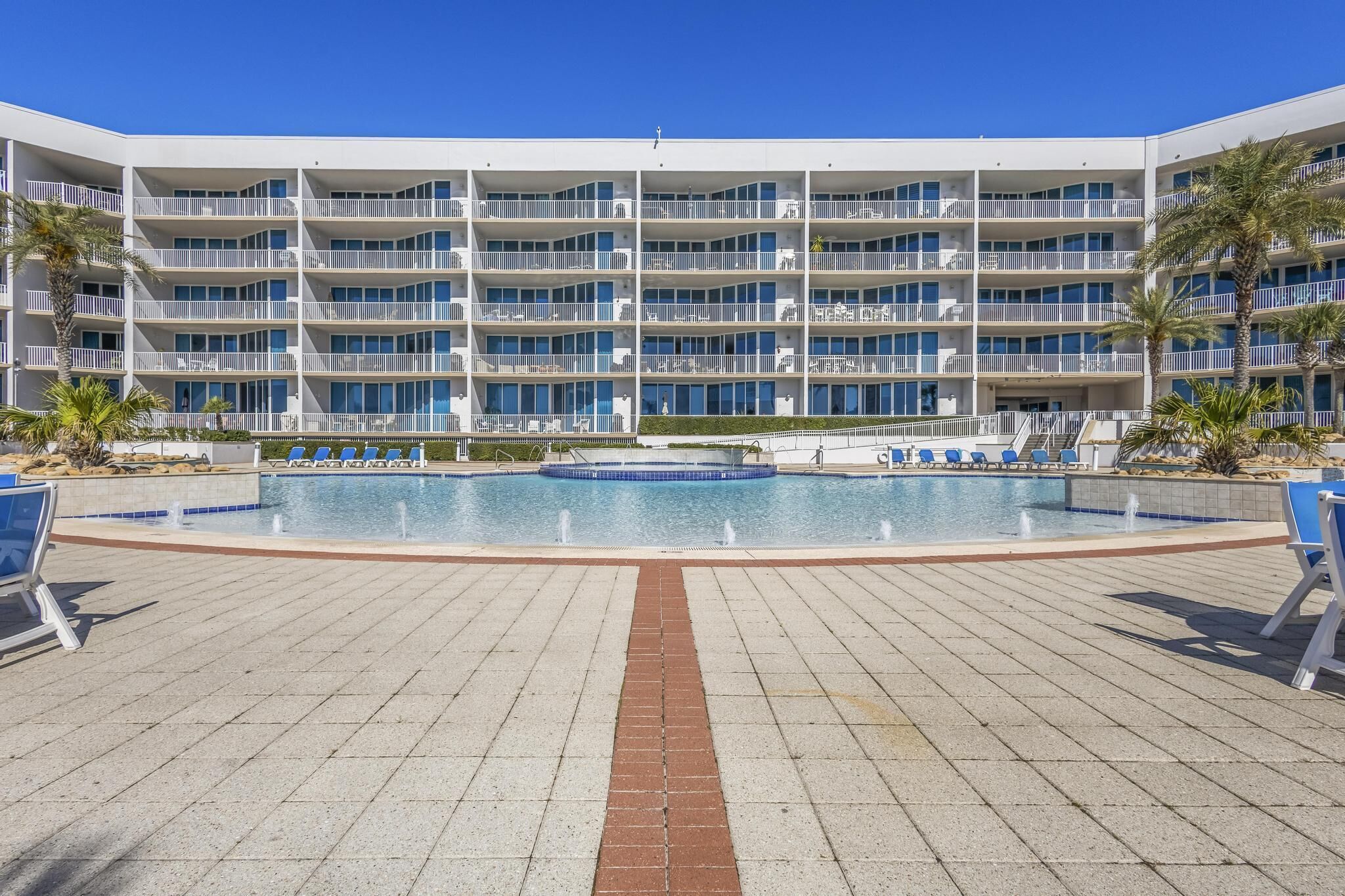 A modern hotel with multiple balconies, a central pool, and sun loungers.