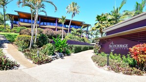 A hotel entrance with a landscaped pathway, palm trees, and a building with balconies. - Anchorage 3, Anchorage 3 on Hamilton Island (Hamilton Island)