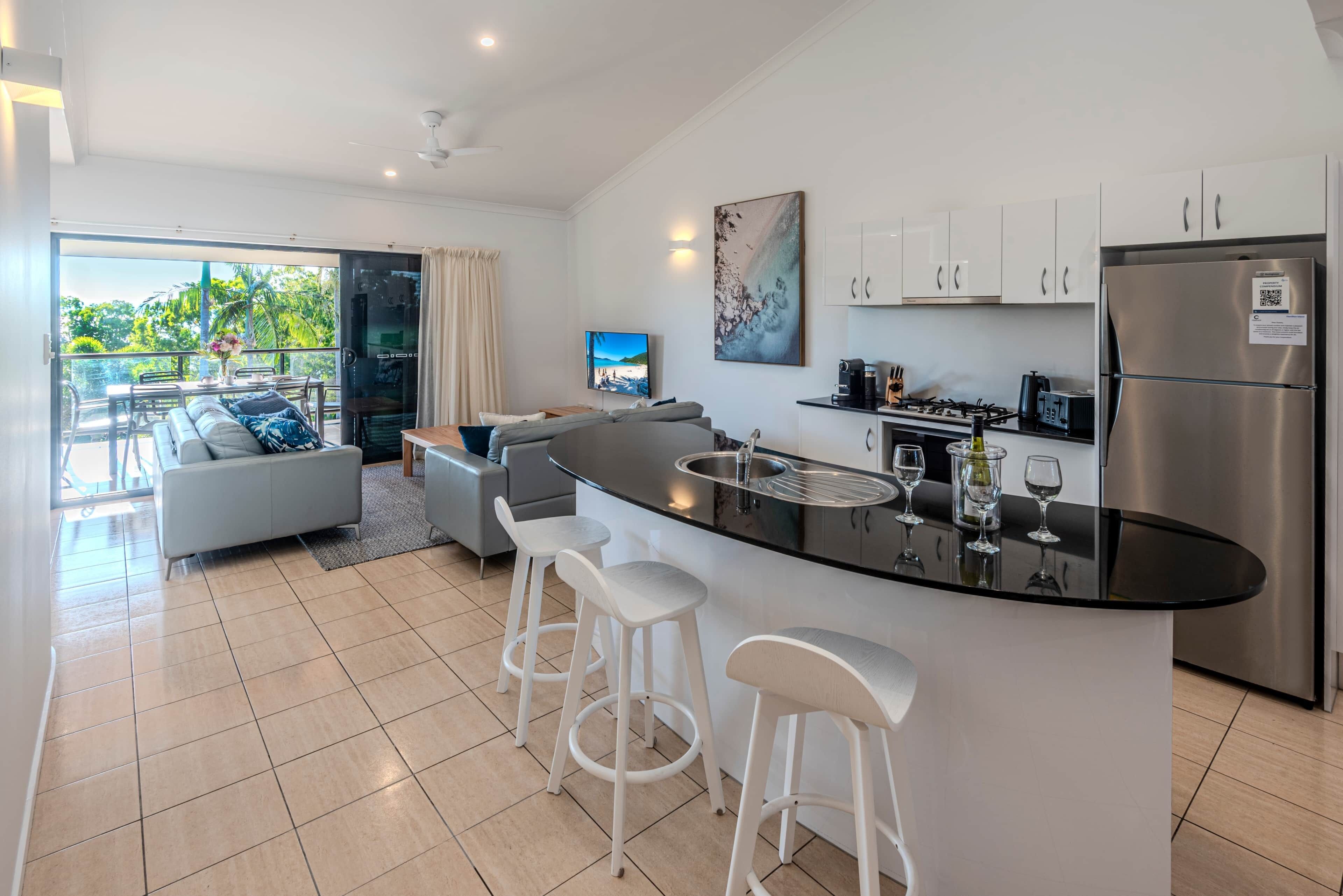 A modern kitchen with a central island, bar stools, and a dining area with a sofa and table.