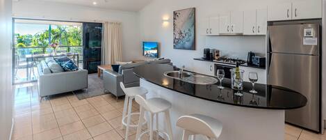 A modern kitchen with a central island, bar stools, and a dining area with a sofa and table.