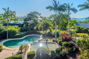 Una piscina rodeada de exuberante vegetación y palmeras, con una vista despejada del mar al fondo.