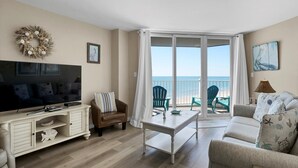 Ein Wohnzimmer mit Fernseher, Couch, Couchtisch und einem Balkon mit Sitzgelegenheiten.