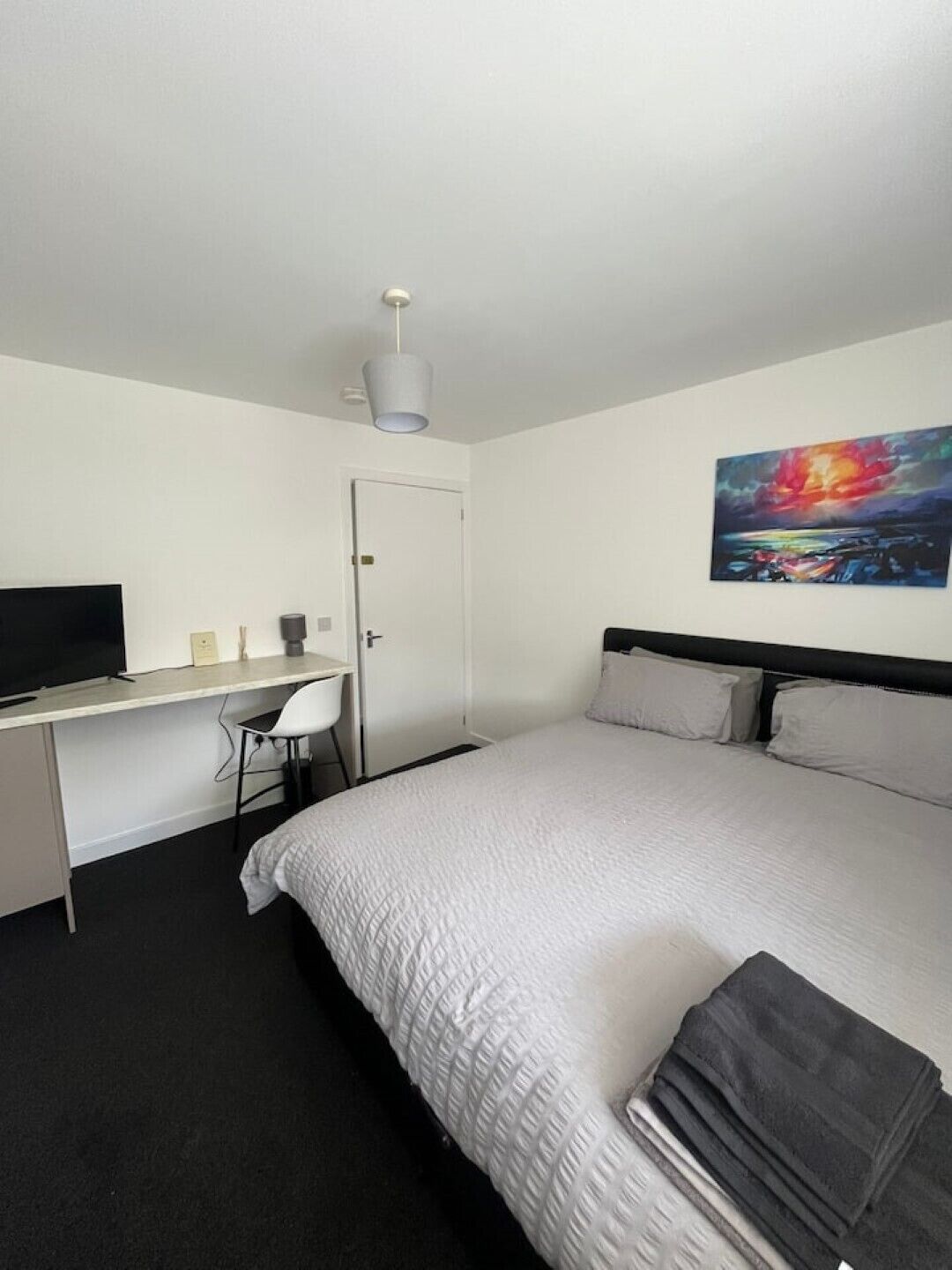 A hotel room with a bed, a desk with a chair, a television, and a painting on the wall.