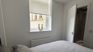 A bedroom with a large bed, a window, a radiator, and a door. - The M Rooms (Shotts)