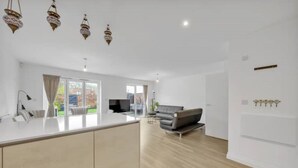 Eine moderne Küche mit Kochinsel, ein Essbereich mit Sofa und ein Wohnzimmer mit Fernseher.