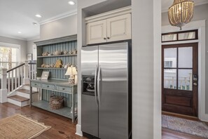 Une cuisine équipée d’un réfrigérateur en acier inoxydable, d’un escalier en bois et d’une étagère décorative ornée de coquillages.