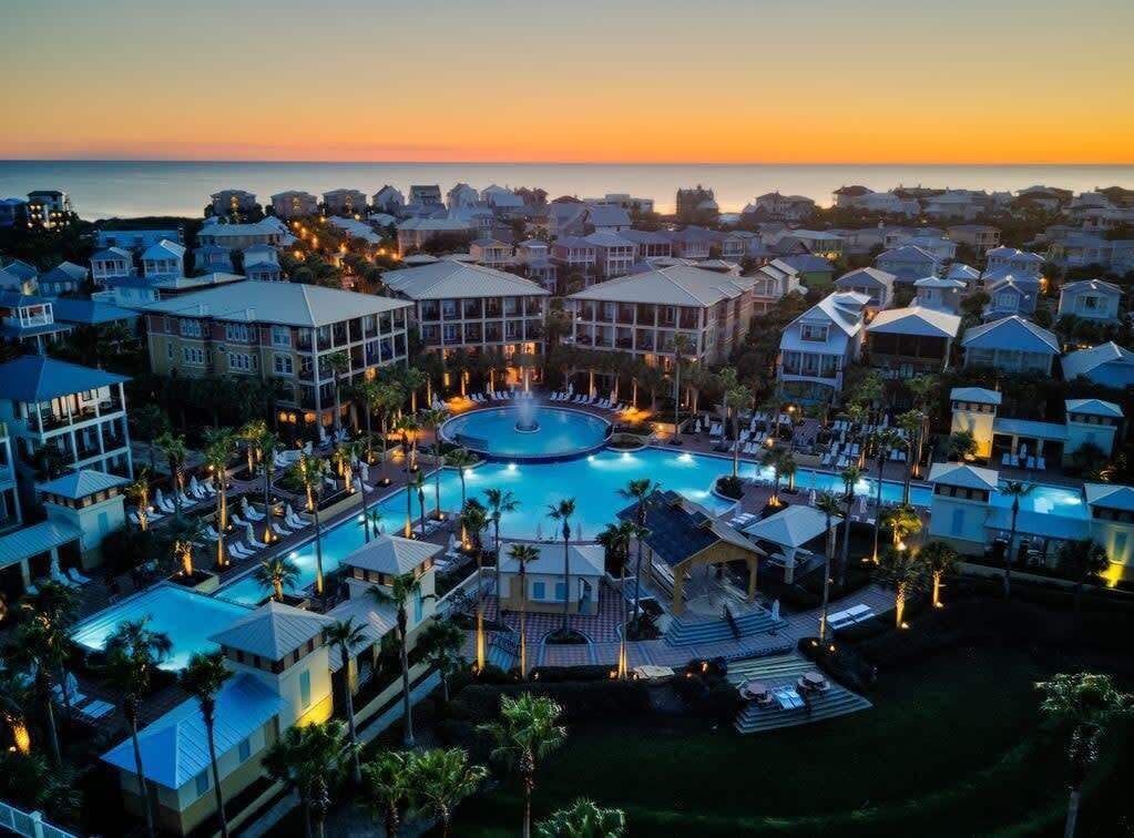 A resort with a central pool, multiple buildings, and a view of the ocean at sunset.