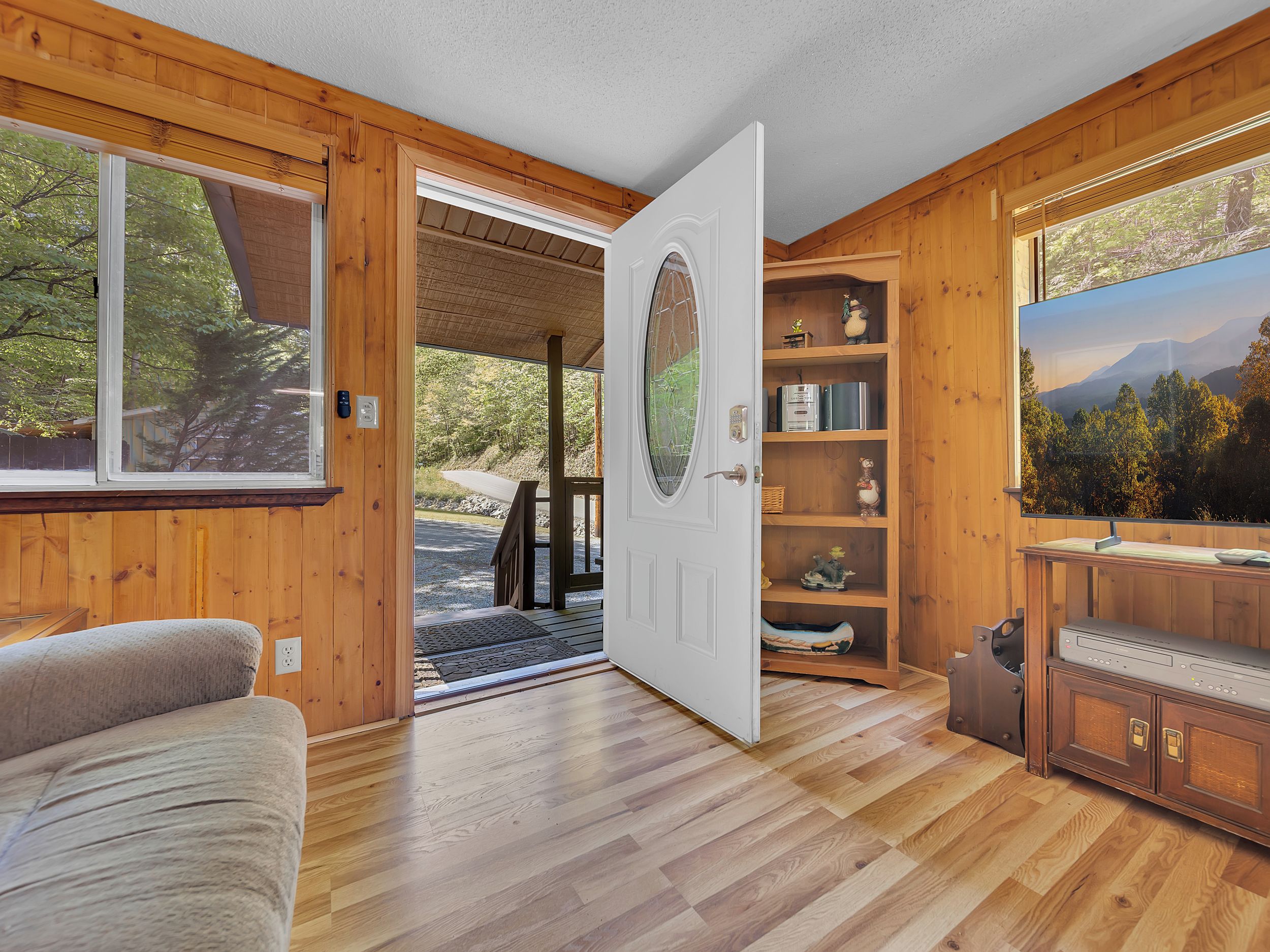 A wooden interior with a door leading to an outdoor area, a built-in shelf with decorative items, and a television.