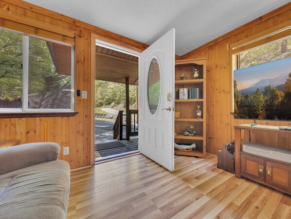 A wooden interior with a door leading to an outdoor area, a built-in shelf with decorative items, and a television.