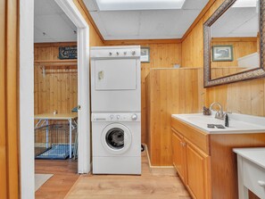 Un cuarto de lavandería con lavadora y secadora apiladas, paredes de madera, un lavabo y un espejo.
