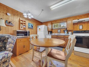 Una cocina tipo cabaña con paredes de madera, una mesa de comedor, sillas, un microondas, un refrigerador, una estufa y una lámpara en el techo.