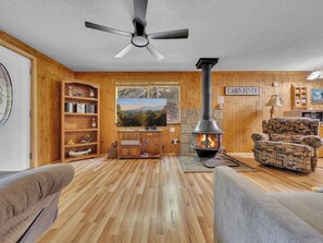 Un interior de cabaña acogedor con estufa de leña, muebles de madera y un amplio ventanal con vistas panorámicas.