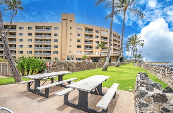 Ein mehrstöckiges Hotel mit Balkonen, eine gepflasterte Terrasse mit Picknicktischen und Blick aufs Meer.