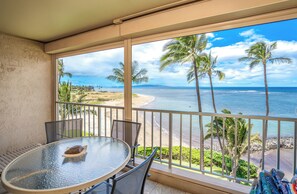 Ein Balkon mit Glastisch und Stühlen, der Blick auf einen Strand mit Palmen und das Meer bietet.