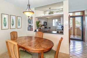 Uma área de refeições com mesa e cadeiras de madeira, luminária pendente e arte com folhas emolduradas na parede.