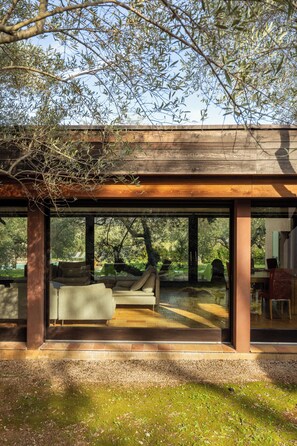 A modern house with large glass windows, a wooden deck, and a view of a garden. - Renovated 7 BR Villa, Garden, Pool & Cannes 30 minutes away (Callian)
