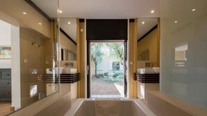 Un baño moderno con una bañera grande, cabina de ducha de vidrio y vistas al jardín.