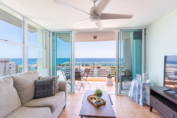 Open, airy space with large windows, ocean views, comfortable seating, and a TV.