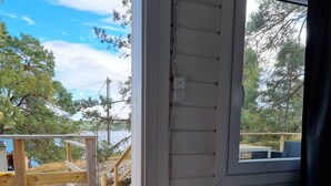 Makuuhuone, jossa on ulkona puinen terassi, ikkuna ja sängyssä ruutukuviollinen päiväpeite.