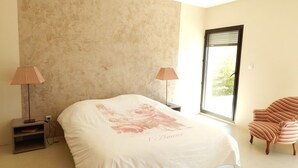 A bedroom with a large bed, two bedside lamps, a window, and a striped chair.