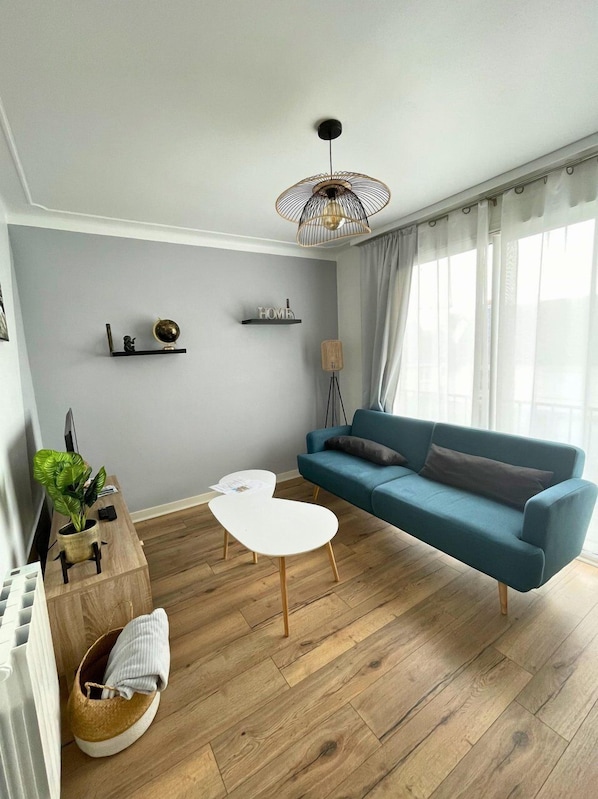 A modern living room with a blue sofa, a white coffee table, a wooden floor, a ceiling fan, and a wall-mounted shelf with decorative items.