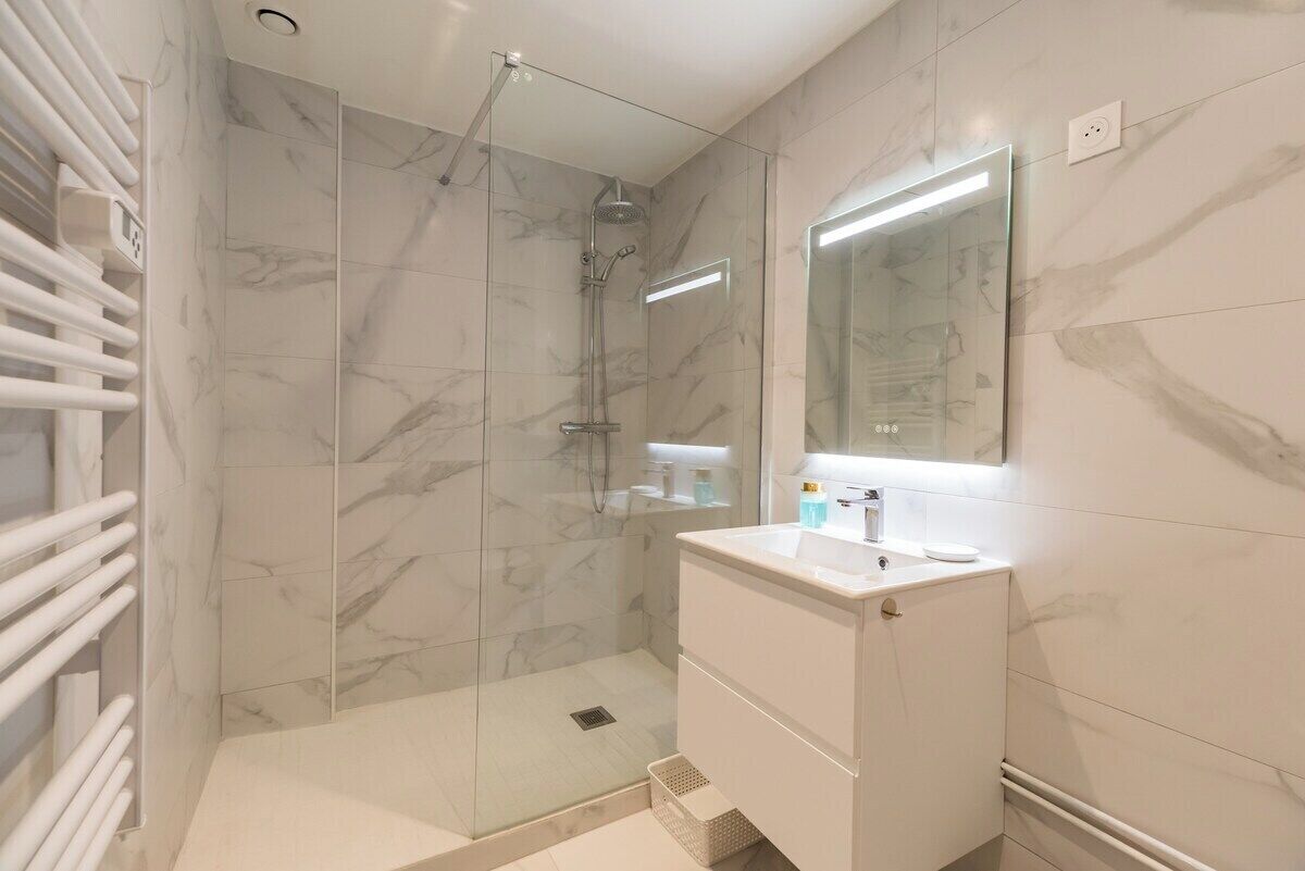 A modern bathroom with a glass-enclosed shower, white marble tiles, and a white vanity with a mirror.