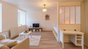 A modern, minimalist living room with a sofa, coffee table, TV, and a desk. - Studio Cosy - plein coeur de Lannion (Lannion)