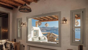 A cozy living room with a large window overlooking a scenic view of mountains and the sea. - Ocean whisper villa with amazing view  (mykonos)