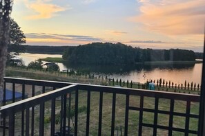 Vista al lago desde una terraza con barandal de madera, un pequeño muelle y un área verde con árboles.