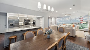 Una cocina moderna con electrodomésticos de acero inoxidable, un comedor con mesa y sillas de madera, y una sala de estar con sofá y un mural de un faro.