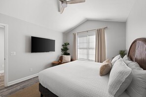 A bedroom with a large bed, a ceiling fan, a TV mounted on the wall, a window with blinds, and a potted plant. - Beach Haven 3BR 2bath (Panama City Beach)